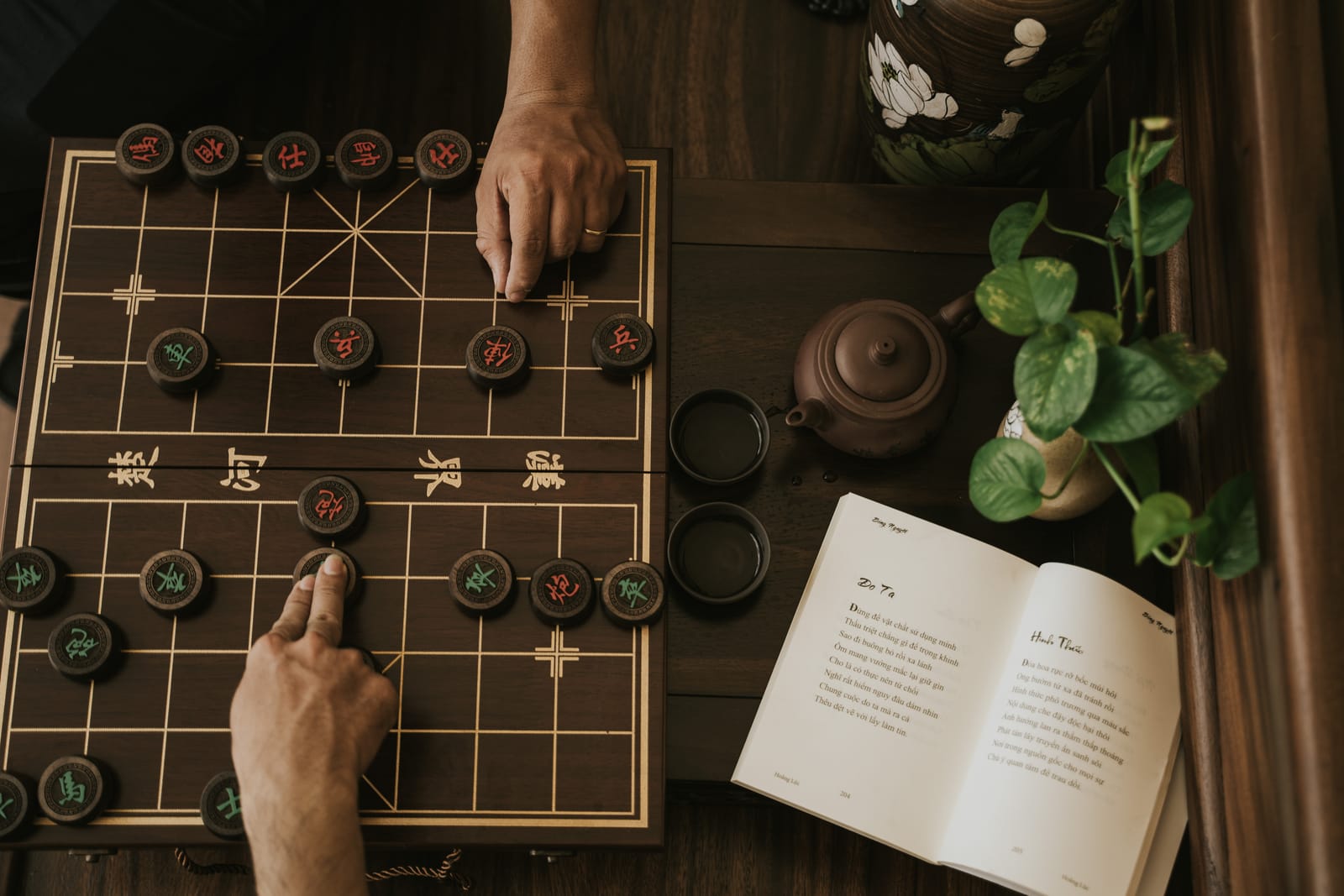 Một nước cờ trên bàn cờ tướng, cuốn thơ mở sẵn bên cạnh.